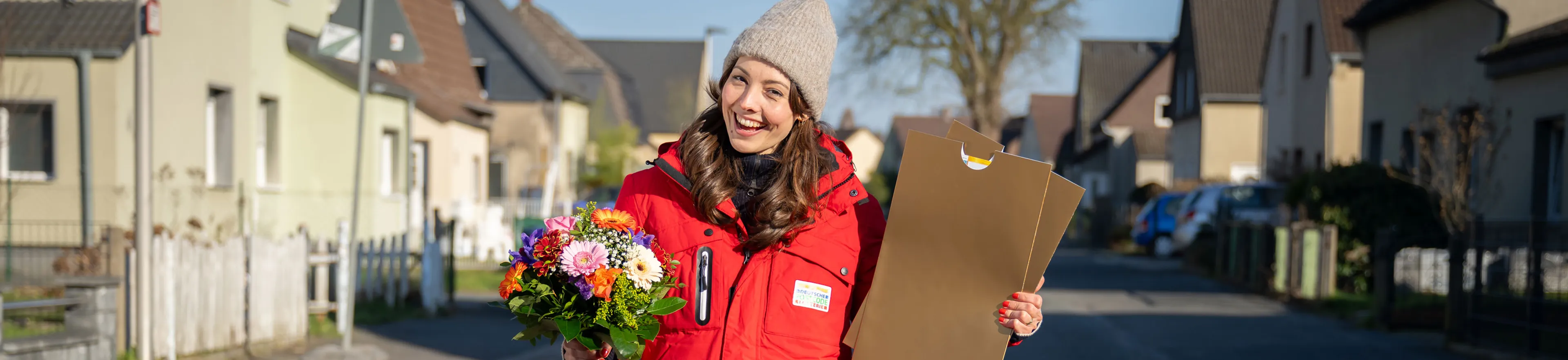 Moderatorin Julia hält Blumen und zwei goldene Umschläge in die Kamera