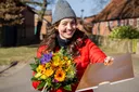 Moderatorin Julia hält einen Blumenstrauß und einen goldenen Umschlag in die Kamera