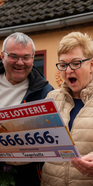 Älteres Paar steht draußen und liest begeistert einen großen Lottoscheck, beide lächeln breit und wirken überrascht.